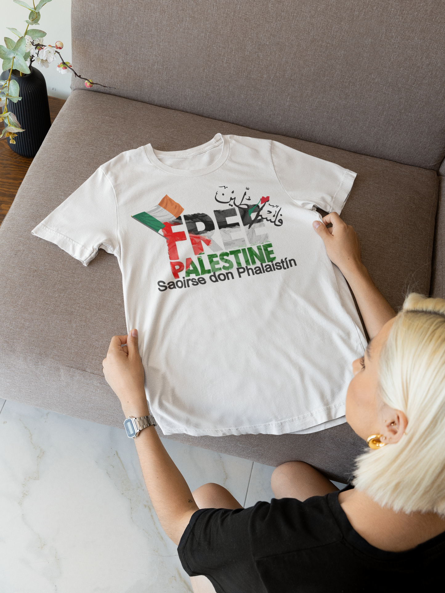 Person holding a white t-shirt with colorful text on a couch